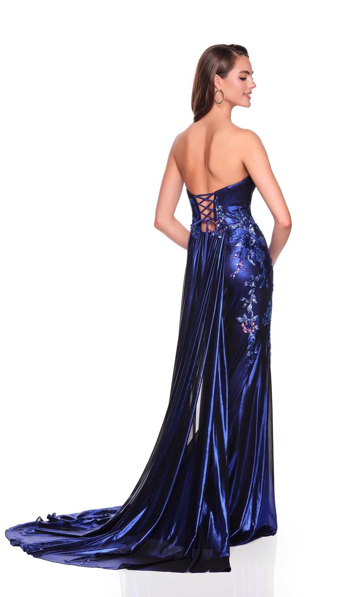 A woman in the Dave and Johnny 12568 long prom dress, featuring a strapless metallic-blue design with floral details and a lace-up back, stands looking to the side.